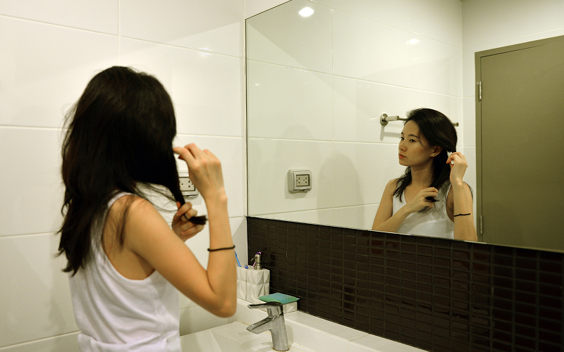 An image of a woman looking at the mirror while observing her hair.