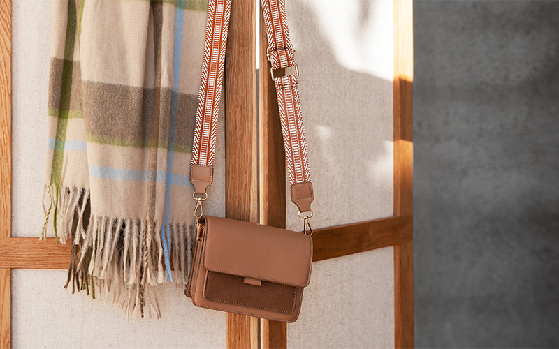 handbag resting on a chair with clothes hanging in the background