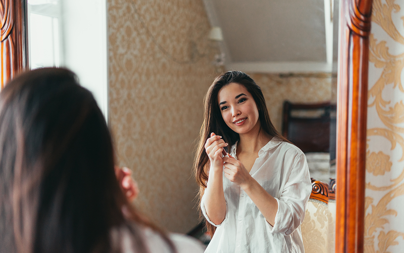 person softly smiling at their reflection in a mirror